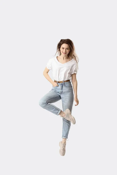 Hoppande ung kvinna i jeans på vit bakgrund — Stockfoto