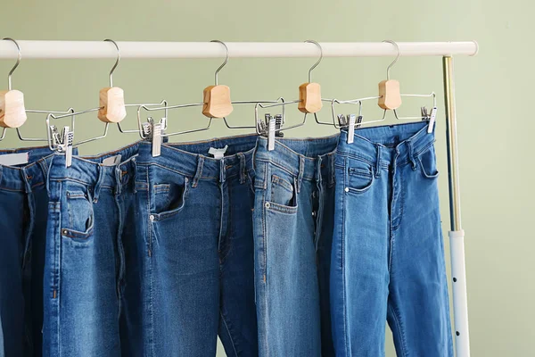 Cremalheira de roupas com calças jeans elegantes diferentes no fundo de cor — Fotografia de Stock