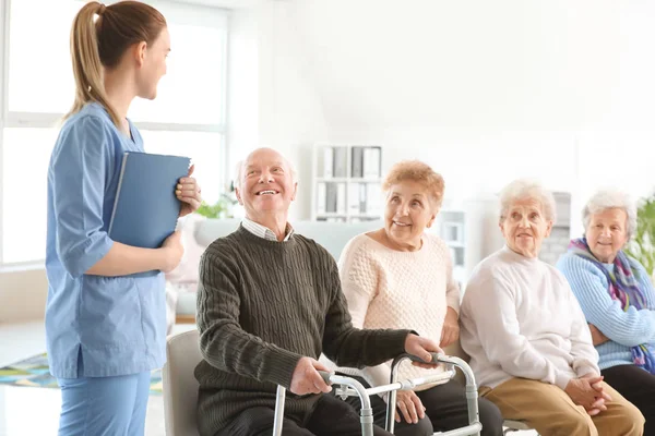 Young caregiver with group of senior people in nursing home — Stock Photo, Image