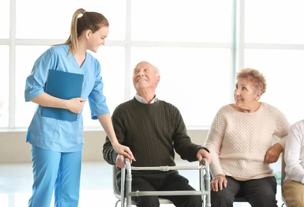 Young caregiver with group of senior people in nursing home — Stock Photo, Image