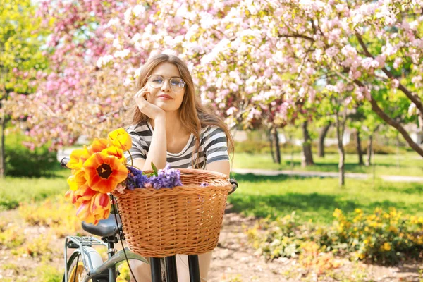 Mulher bonita com bicicleta e flores no parque no dia de primavera — Fotografia de Stock