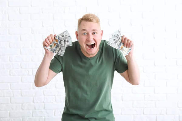 Happy young man with dollar banknotes on white brick background — Stock Photo, Image