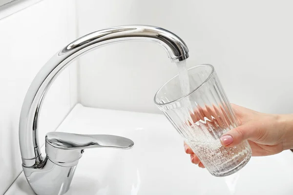 Woman filling glass with water from kitchen faucet