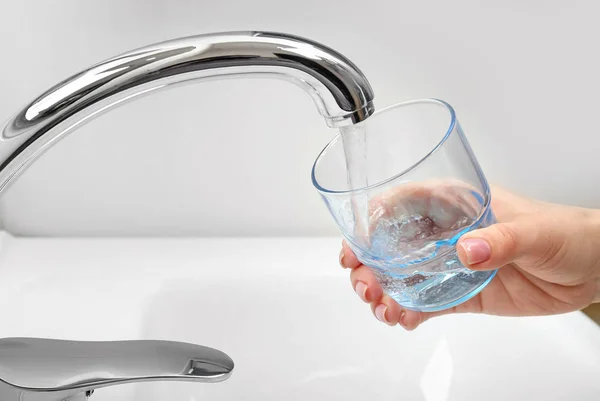 Woman filling glass with water from kitchen faucet