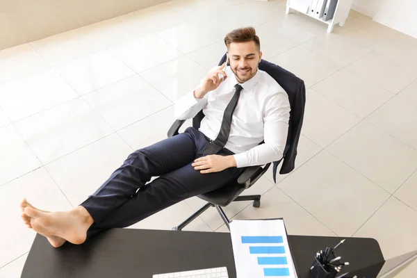 Carefree businessman talking by mobile phone in office — Stock Photo, Image