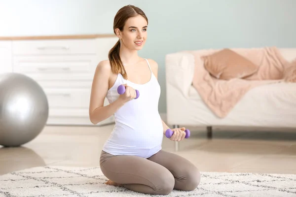 Beautiful pregnant woman with dumbbells training at home — Stock Photo, Image