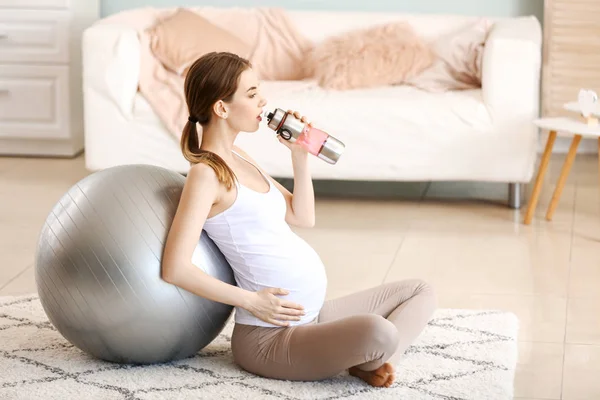 Красивая беременная женщина пьет воду во время тренировки дома — стоковое фото
