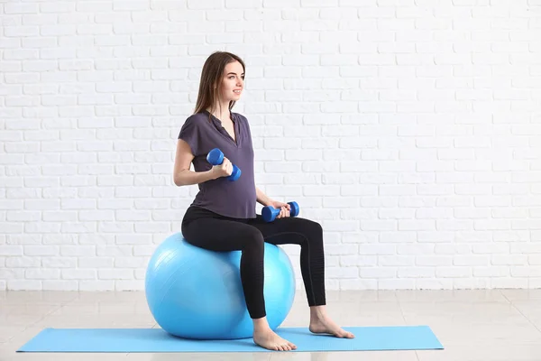 Mulher grávida bonita com halteres e treinamento fitball perto da parede de tijolo branco — Fotografia de Stock