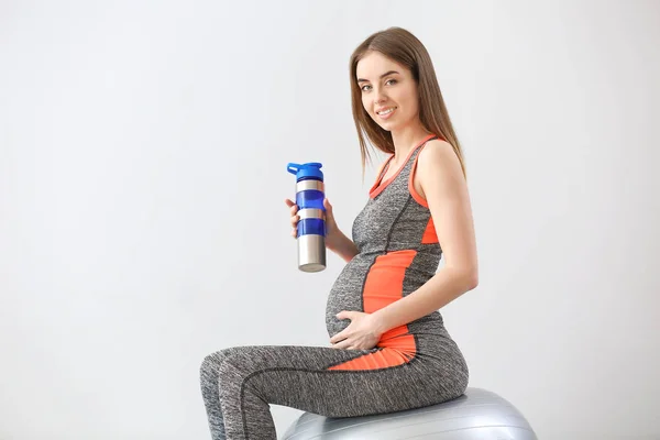 Beautiful sporty pregnant woman drinking water during training against grey background — Stock Photo, Image