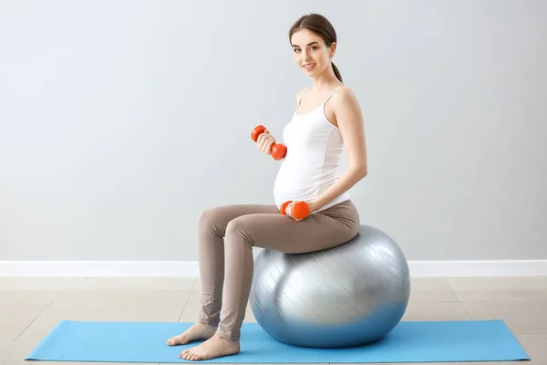 Beautiful pregnant woman with dumbbells and fitball training near grey wall — Stock Photo, Image