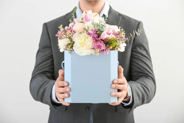 Handsome man with bouquet of beautiful flowers on light background