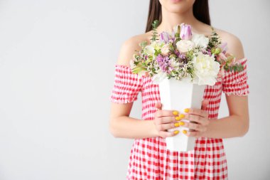 Açık arkaplanda bir buket çiçekle güzel bir genç kadın.