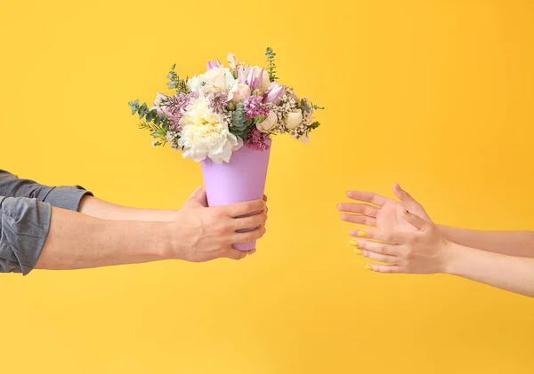 Man giving flowers to woman on color background