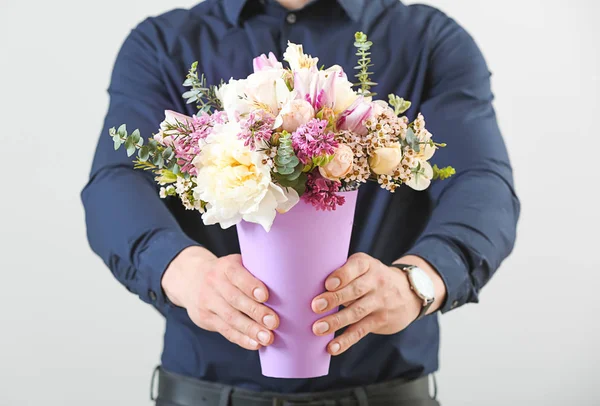 Schöner Mann mit einem Strauß schöner Blumen auf hellem Hintergrund — Stockfoto