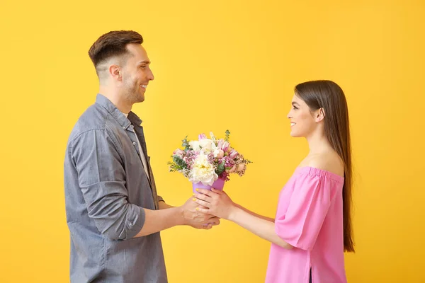 Mujer recibiendo flores de hombre joven sobre fondo de color — Foto de Stock
