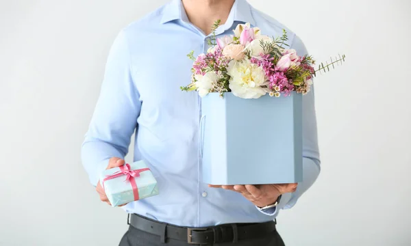 Handsome man with bouquet of beautiful flowers and gift box on light background