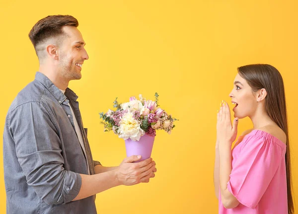 Man giving flowers to surprised woman on color background