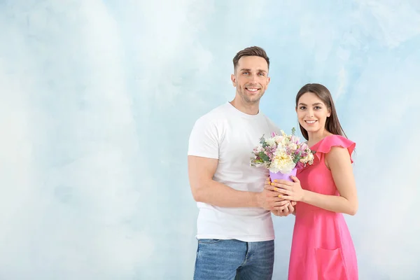 Young couple with bouquet of beautiful flowers on light background — Stock Photo, Image