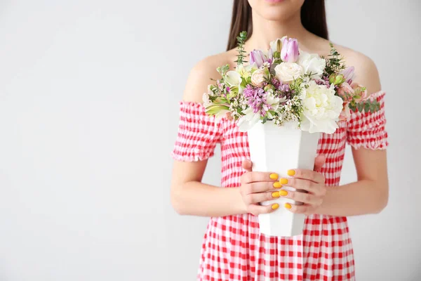 Bella giovane donna con mazzo di fiori su sfondo chiaro — Foto Stock