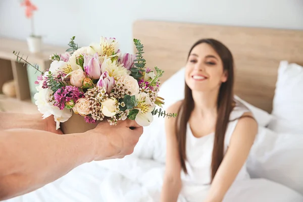 Marido saludando a su esposa con ramo de flores en el dormitorio en casa — Foto de Stock