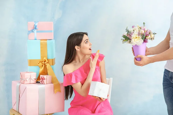 Man giving flowers to surprised woman on color background — Stock Photo, Image