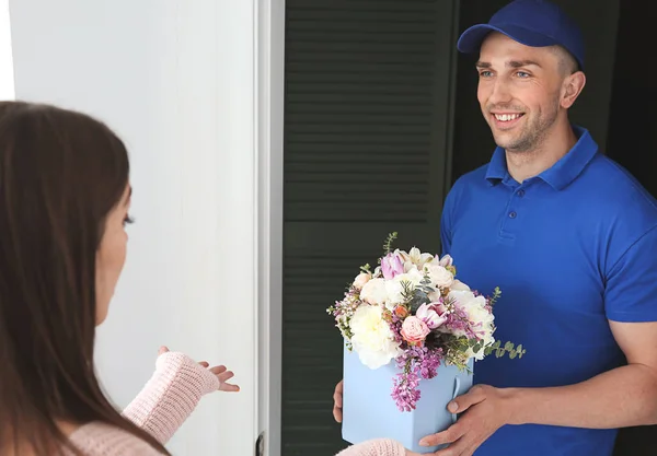 Mujer joven que recibe hermosas flores de entrega hombre en casa — Foto de Stock