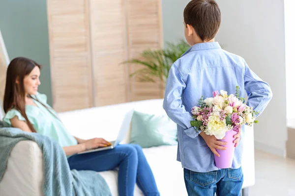Kleine jongen verbergen van bloemen voor zijn moeder achter terug thuis — Stockfoto