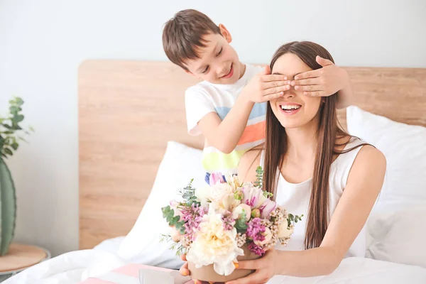 Little son greeting his mother with bouquet of flowers in bedroom at home — Stock Photo, Image