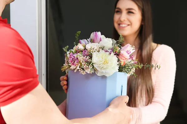 Young woman receiving beautiful flowers from delivery man at home — Stock Photo, Image