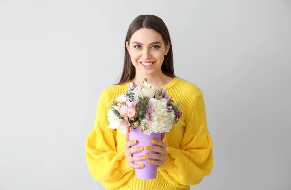 Schöne junge Frau mit Blumenstrauß auf hellem Hintergrund — Stockfoto