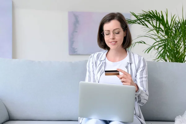 Ung kvinna med kreditkort och laptop shopping på nätet hemma — Stockfoto