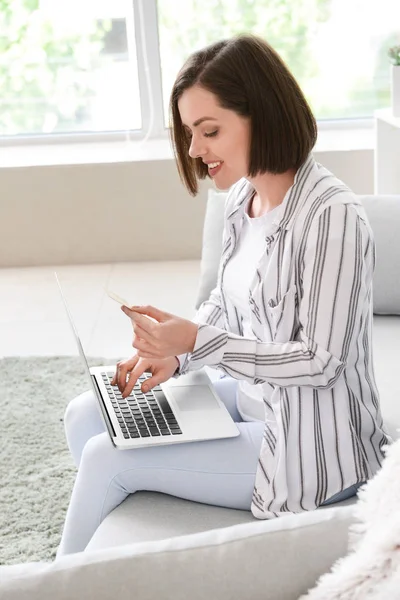 Young woman with credit card and laptop shopping online at home — Stock Photo, Image