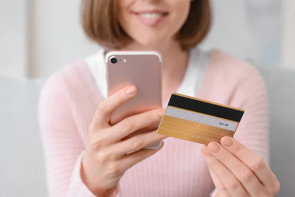 Jeune femme avec carte de crédit et téléphone mobile shopping en ligne à la maison, gros plan — Photo