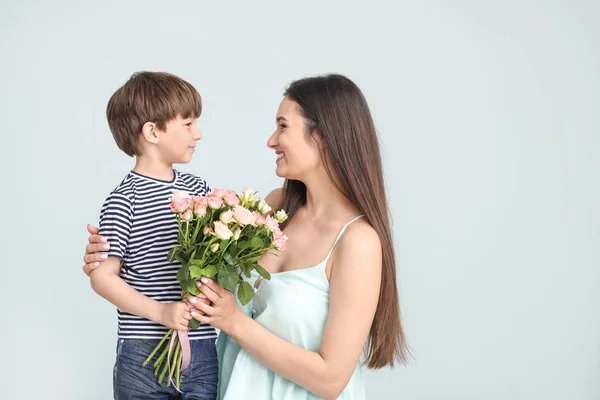 Gelukkige moeder en zoon met boeket bloemen op grijze achtergrond — Stockfoto