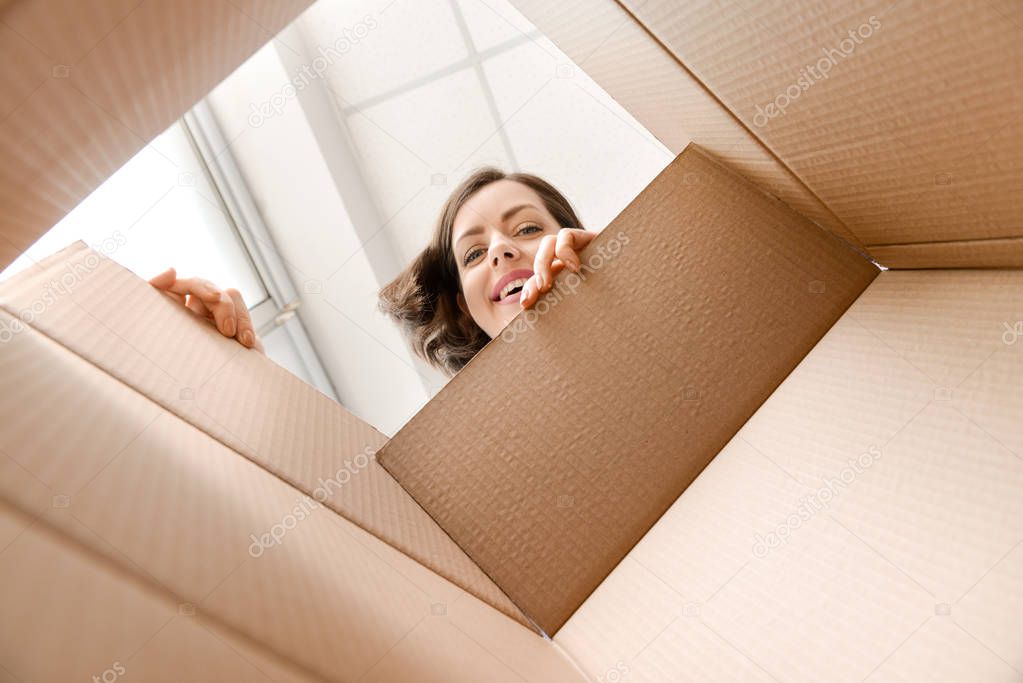 Young woman opening parcel at home, view from inside of box