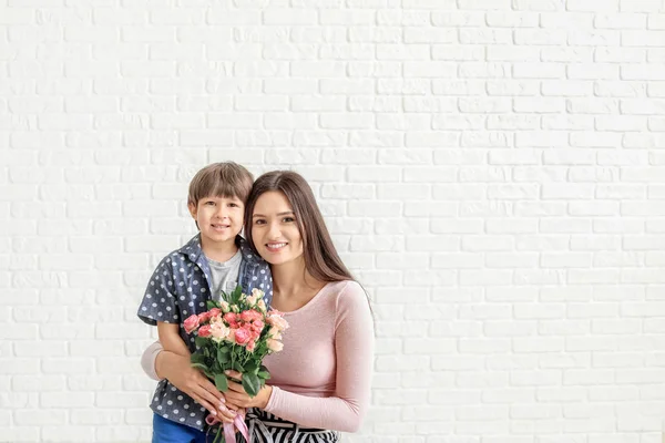 Счастливая мать и сын с букетом цветов на белом кирпичном фоне — стоковое фото