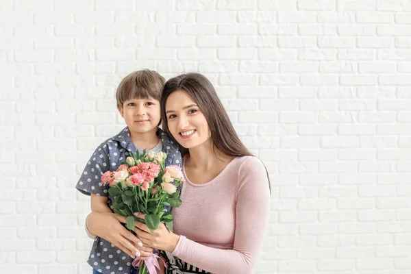 Happy mother and son with bouquet of flowers on white brick background — Stock Photo, Image