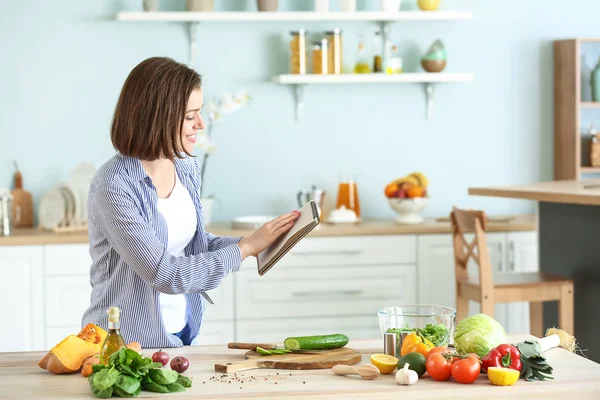 Mujer joven con libro de recetas cocina en la cocina —  Fotos de Stock