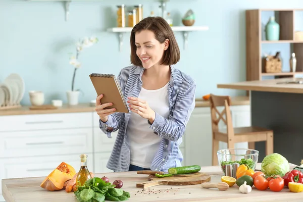 Young woman with recipe book cooking in kitchen — Stock Photo, Image