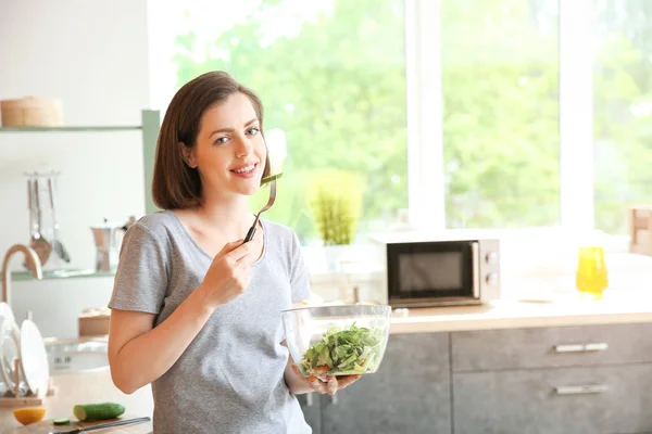 Hermosa mujer joven comiendo ensalada fresca en la cocina —  Fotos de Stock