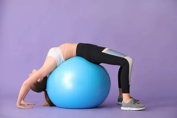 Joven mujer deportiva haciendo ejercicios con fitball sobre fondo de color —  Fotos de Stock