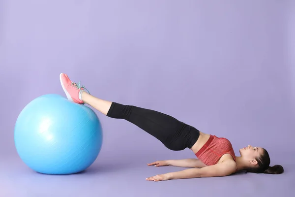 Joven mujer deportiva haciendo ejercicios con fitball sobre fondo de color — Foto de Stock