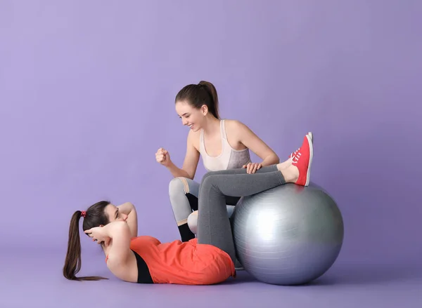 Jonge sportieve vrouw met fitball oefeningen onder supervisie van haar personal trainer op kleur achtergrond — Stockfoto