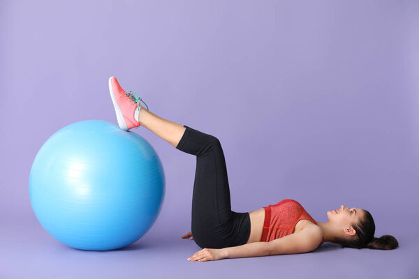 Молодая спортсменка делает упражнения с фитболом на цветном фоне
