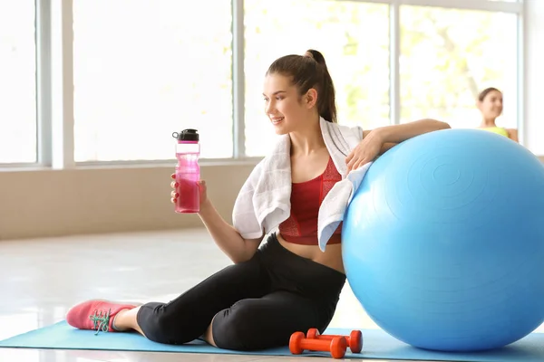 Jovem mulher esportiva com fitball água potável no ginásio — Fotografia de Stock
