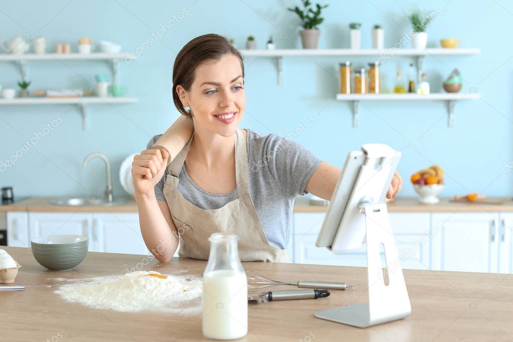 Beautiful young woman with tablet computer cooking pastry in kitchen