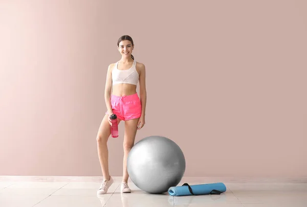 Junge sportliche Frau mit Fitball und Wasserflasche nahe der Farbwand — Stockfoto