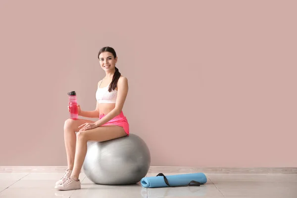 Young sporty woman with fitball and bottle of water near color wall — Stock Photo, Image