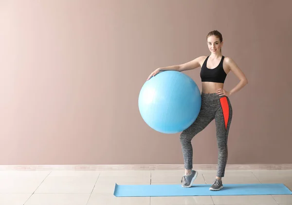 Jovem mulher esportiva com fitball perto da parede de cor — Fotografia de Stock