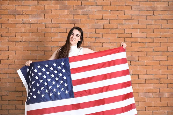 Mujer joven feliz con bandera nacional de EE.UU. sobre fondo de ladrillo — Foto de Stock